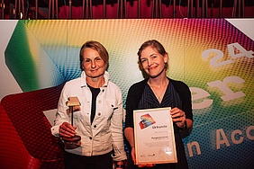 Zwei Frauen, die eine Urkunde und einen Preis in die Kamera halten auf den Enter-Awards 2024.